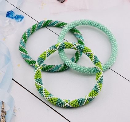 Three handcrafted seed bead bracelets in shades of green, mint, and white, arranged on a light background.